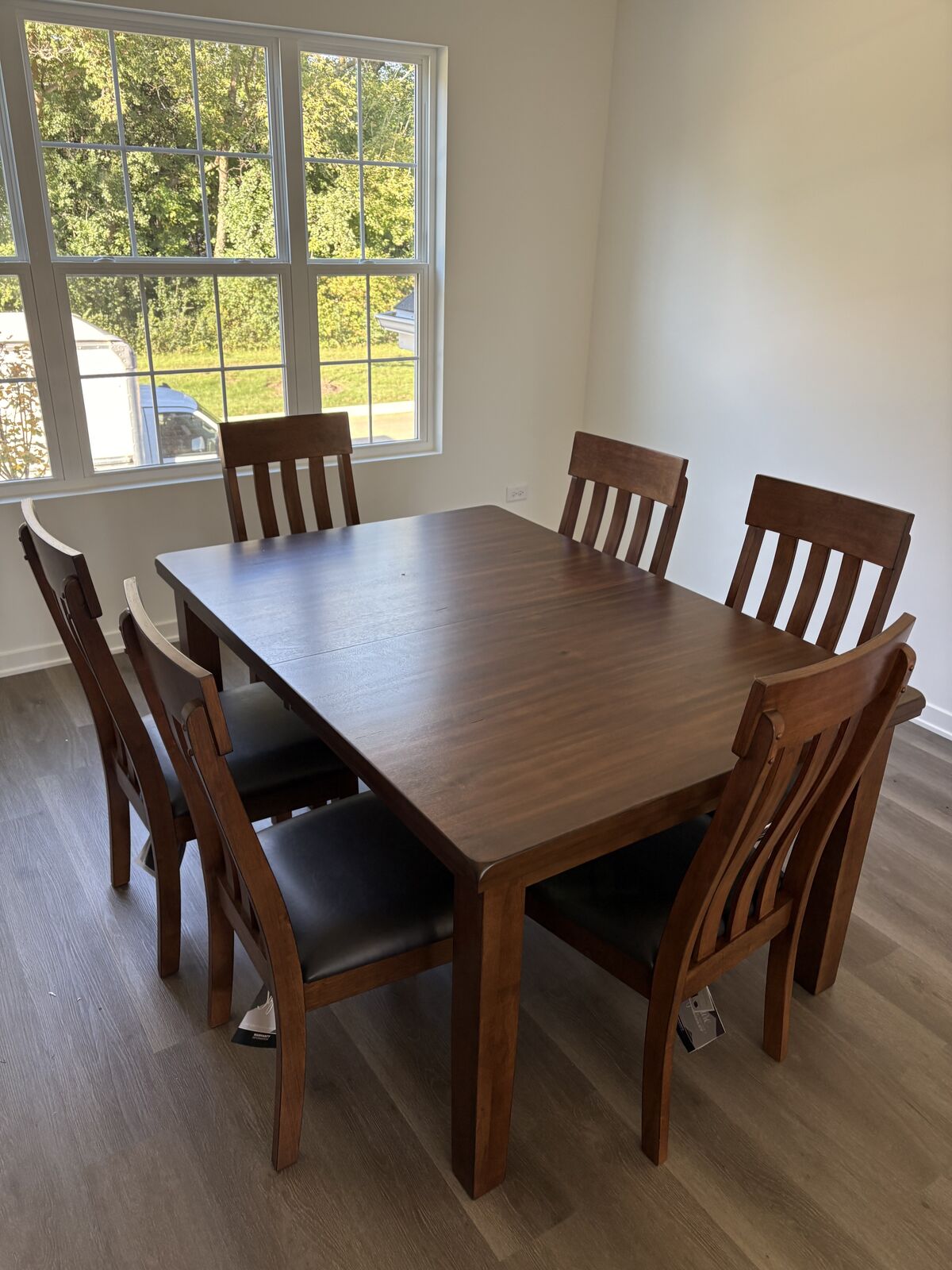 Wood dining table with six upholstered chairs beside a sunny window
